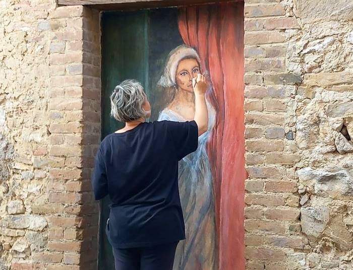 Una donna affacciata alla porta di una casa abbandonata: Tufo di Carsoli si arricchisce di un nuovo murale